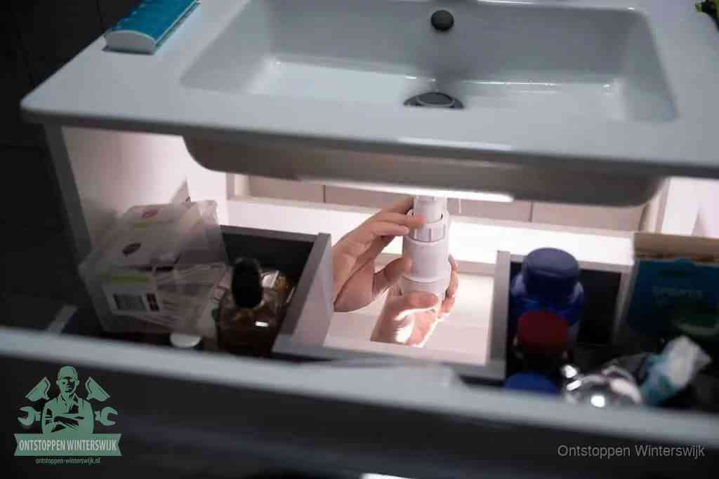 Een pompfles met zeep boven een wastafel, de heet water en afwasmiddel-methode om een vetprop in de afvoer los te maken in Winterswijk