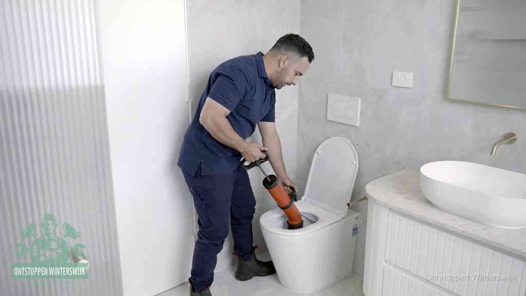 Een monteur buigt over een wandcloset en duwt met de hand een persluchtontstopper in de toiletpot om de verstopping handmatig los te maken in Winterswijk