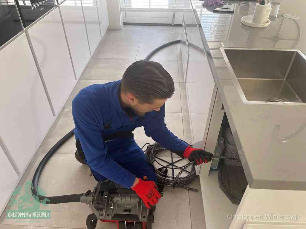 Een monteur ontstopt de keukenafvoer onder de spoelbak met een elektrische veermachine in Winterswijk