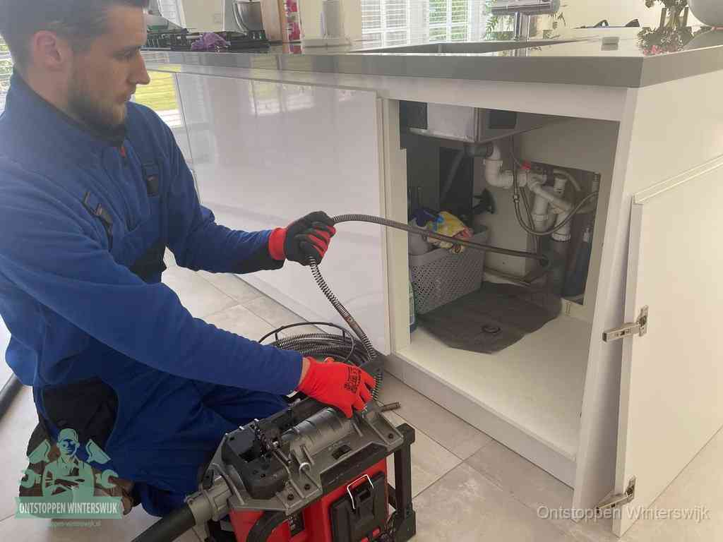 Monteur voert een ontstoppingsveer in de afvoer onder de keuken in Winterswijk