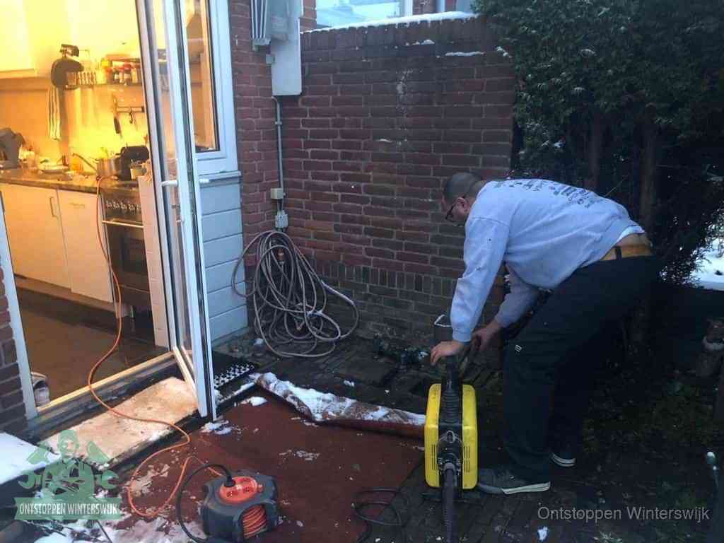 Een monteur werkt buiten bij een open riool-/grondput met een elektrische ontstoppingsmachine om een verborgen afvoerprobleem op te sporen in Winterswijk