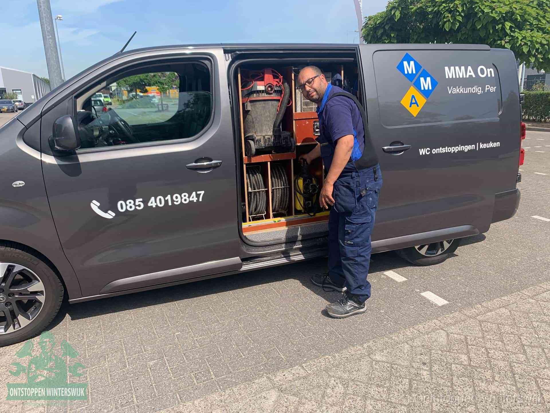Een monteur bij de open schuifdeur van zijn bedrijfsbus op een parkeerplaats, klaar om de oorzaak van terugkerende afvoerverstoppingen aan te pakken in Winterswijk