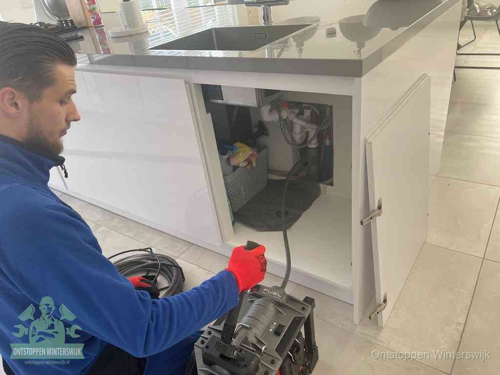 Monteur ontstopt met een veermachine een verstopte afvoer onder de gootsteen in Winterswijk