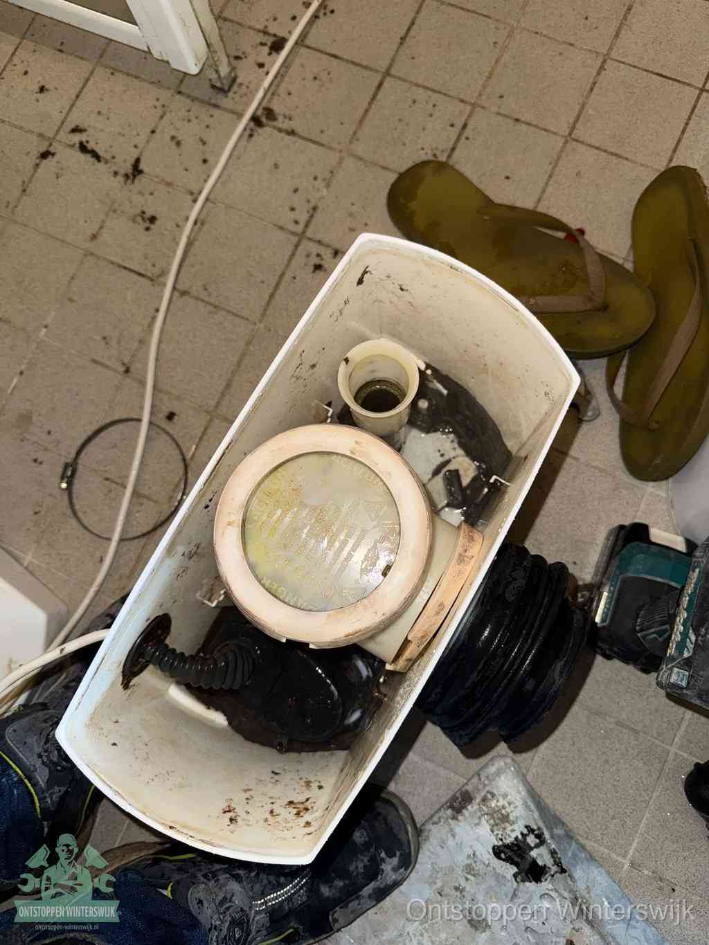 Een gedemonteerde toiletpot op de vloer met ontstoppingsveer en gereedschap ernaast, het verwijderen van een vastzittend voorwerp uit de wc in Winterswijk