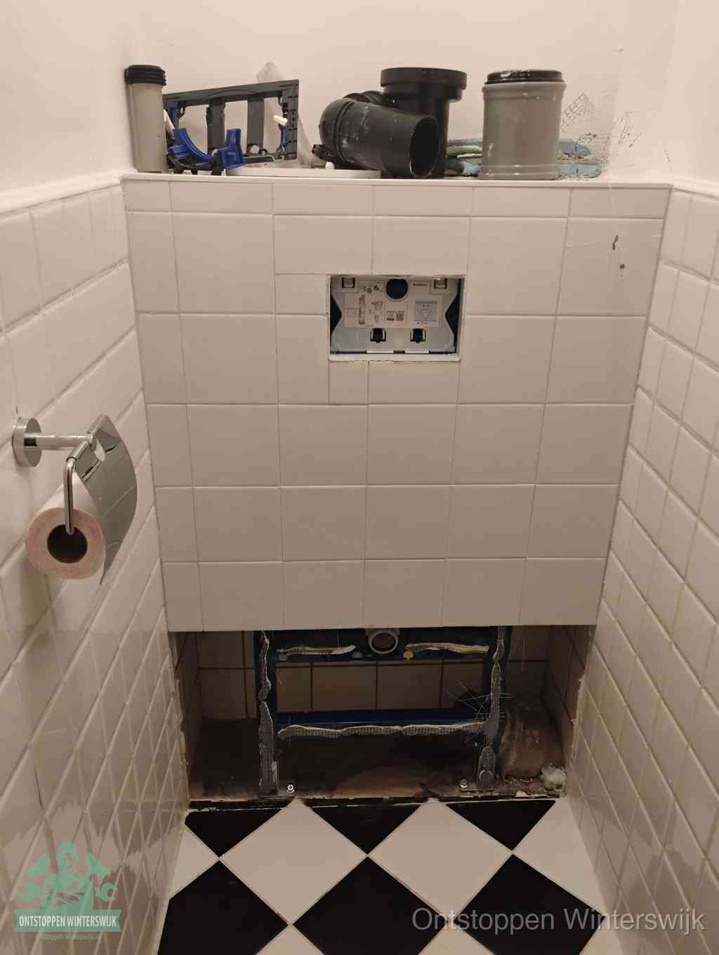 Een toiletruimte waar het hangtoilet en de inbouwreservoir-onderdelen zijn vrijgelegd voor onderhoud, periodiek nazicht voorkomt een wc-verstopping in Winterswijk