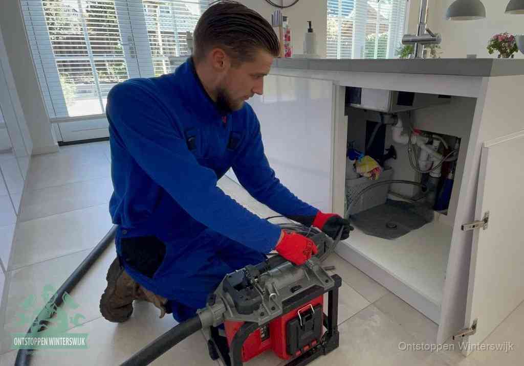 Een monteur voert een professionele elektrische ontstoppingsmachine in de afvoer onder de spoelbak tijdens het gootsteen ontstoppen in Winterswijk