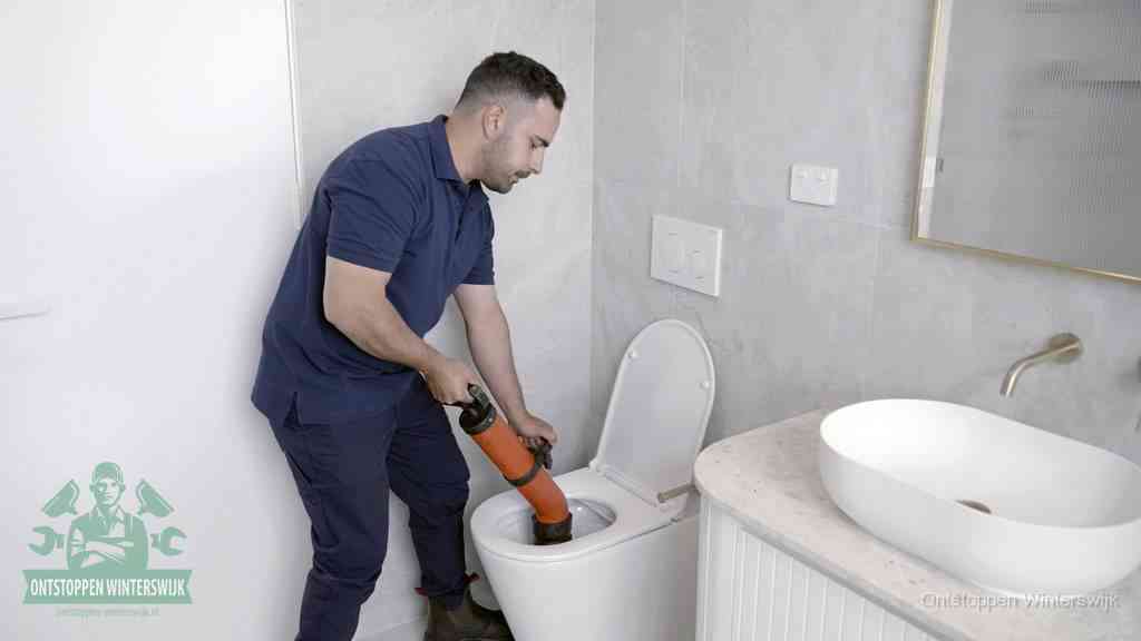 Een man gebruikt een handmatige luchtdruk-ontstopper in een modern betegeld toilet om zelf de wc te ontstoppen in Winterswijk